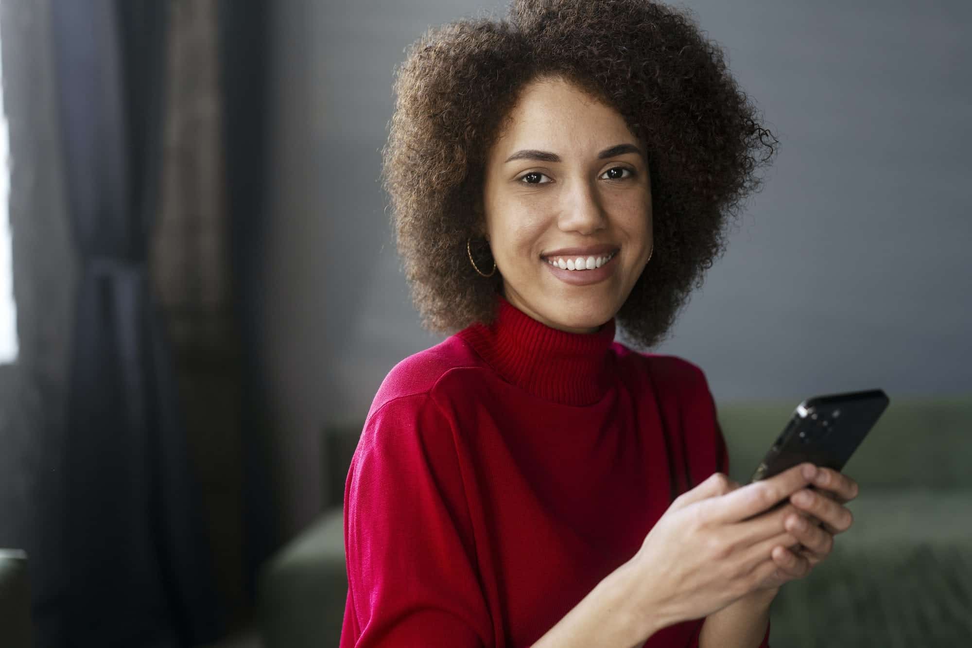 african american woman in red casual attire using mobile phone working online text messaging | Assessoria Araramax